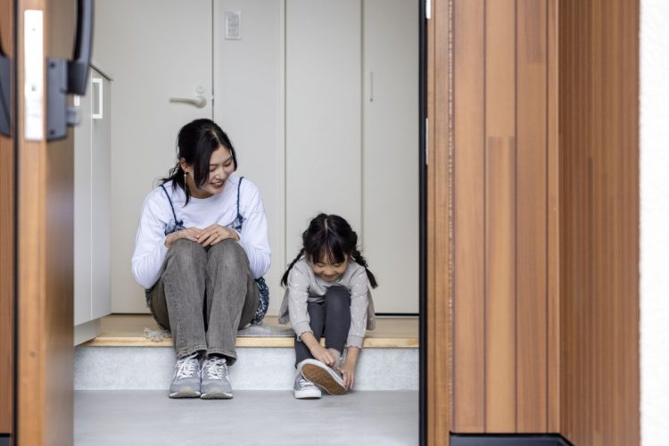 玄関で靴を履く女の子とそれを眺めるお母さん